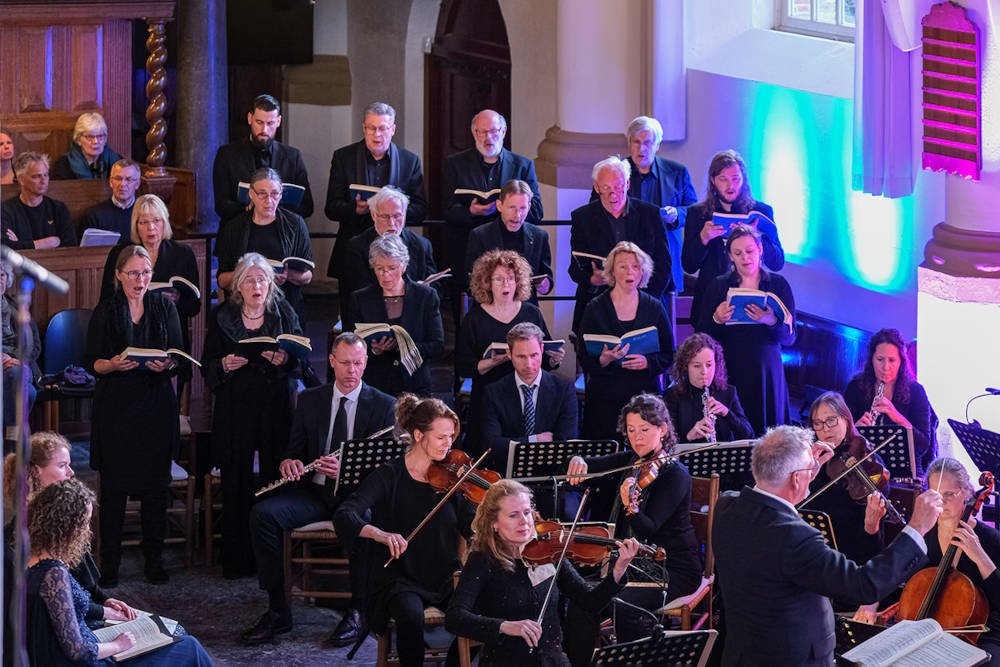 Koor en orkest tijdens de uitvoering in de Hobbe van Baerdtkerk, het koor staand achter de zittende strijkers en blazers.